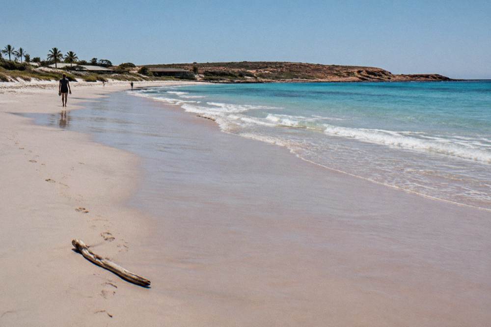 Waves washing onto pale sand at a Ningaloo beach under a clear sky