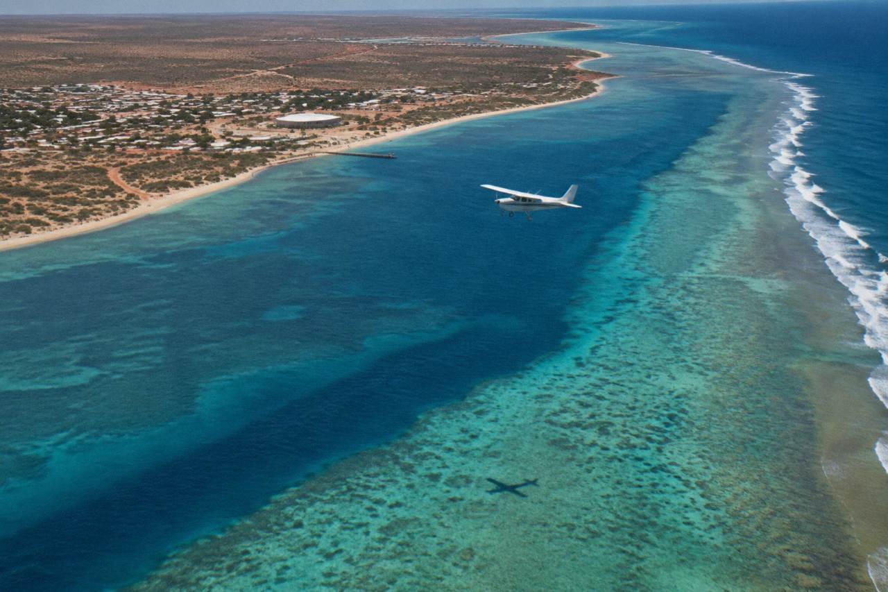 Aerial view of a small plane flying over turquoise ocean water near Ningaloo Reef
