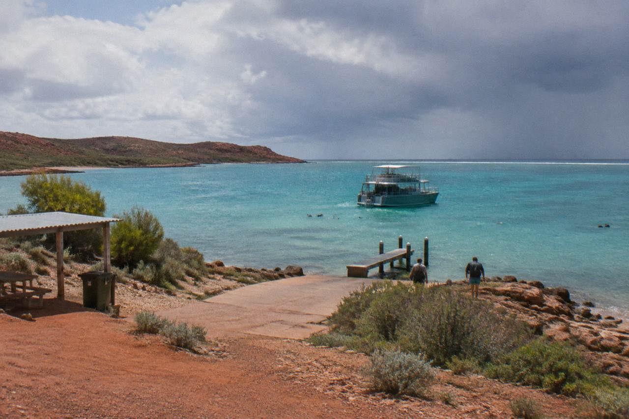 A snorkel boat moored beside the Ningaloo Reef with clear turquoise water and a low reef line on the horizon