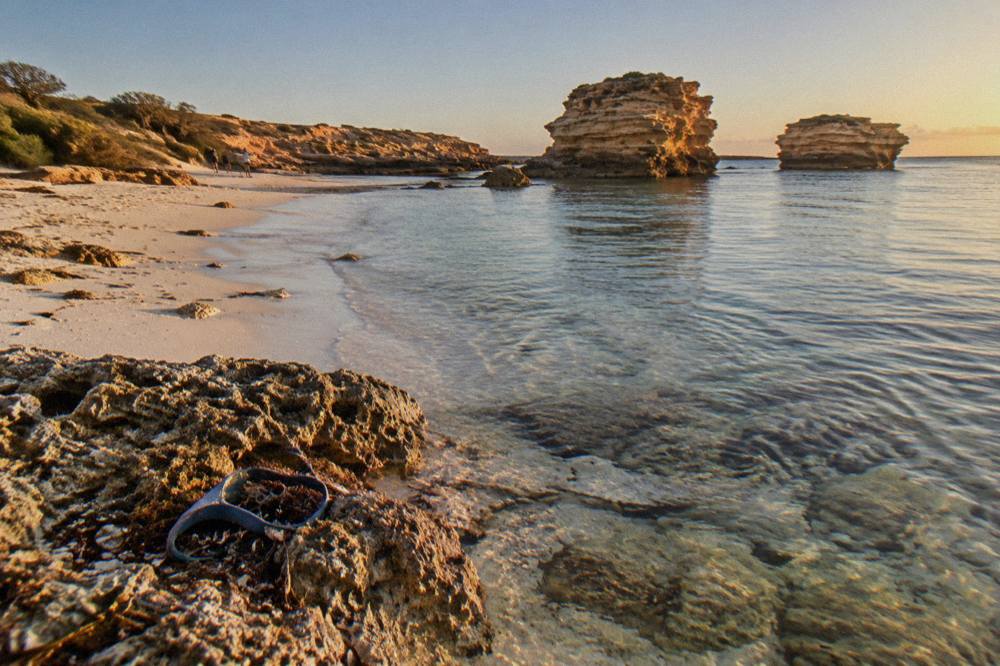 A calm sandy beach with clear shallow water and reef visible below the surface