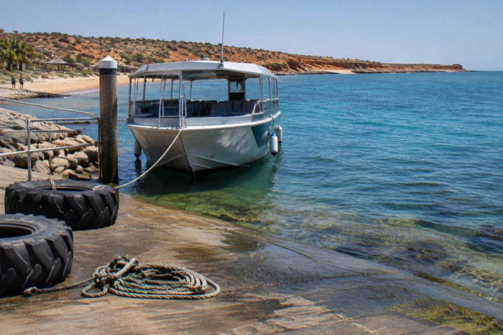 A tour boat anchored beside a coral reef in calm blue water at Ningaloo