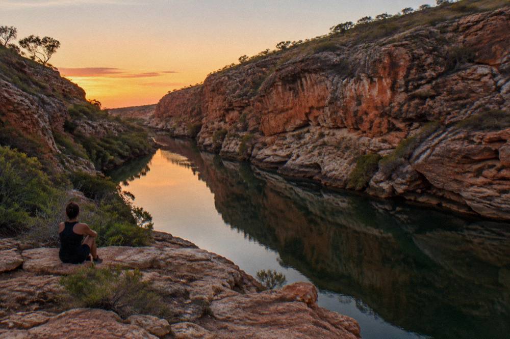 Red rock gorge of Yardie Creek with calm water and low scrub on the cliffs