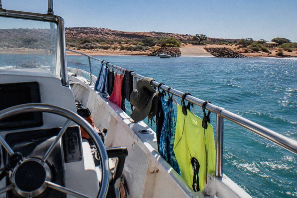 Rash vests, hats and towels drying on the rail of a tour boat in bright sunshine