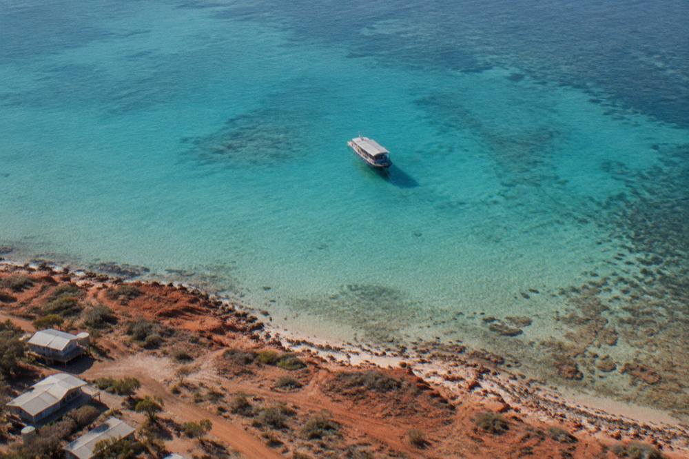 A tour boat anchored near the Ningaloo reef edge with clear water and distant coastline