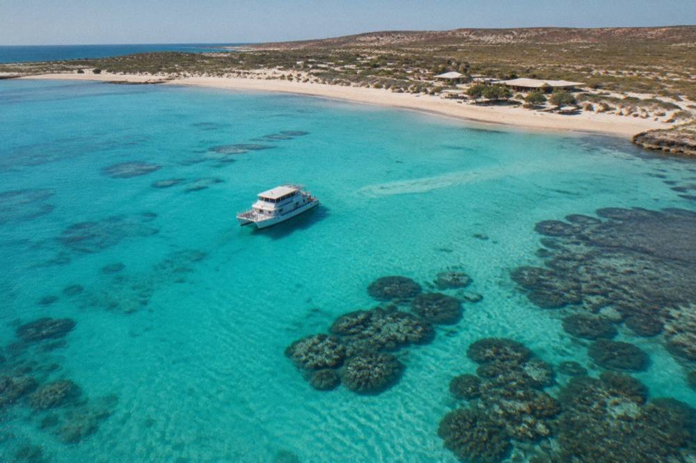 A tour boat anchored beside a coral reef in clear turquoise water at Ningaloo