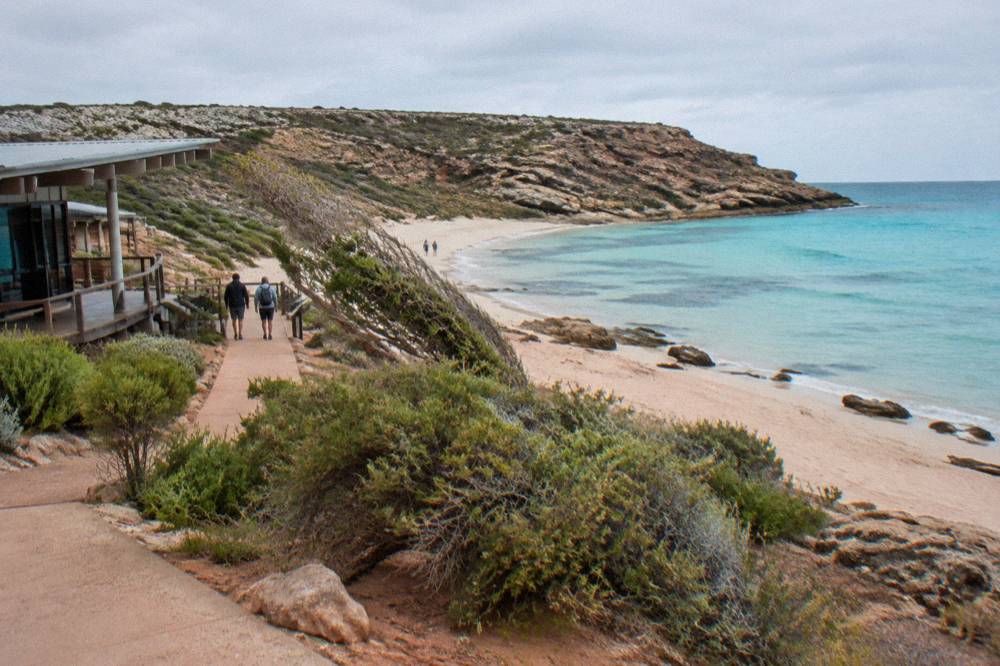 A white sandy beach with clear turquoise shallows and rocky headland at one end