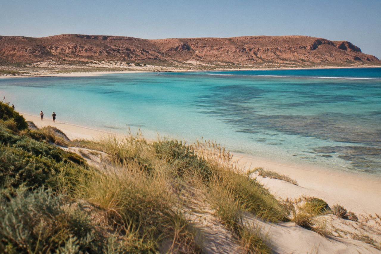 Red limestone range rising above a pale sandy beach beside turquoise reef water