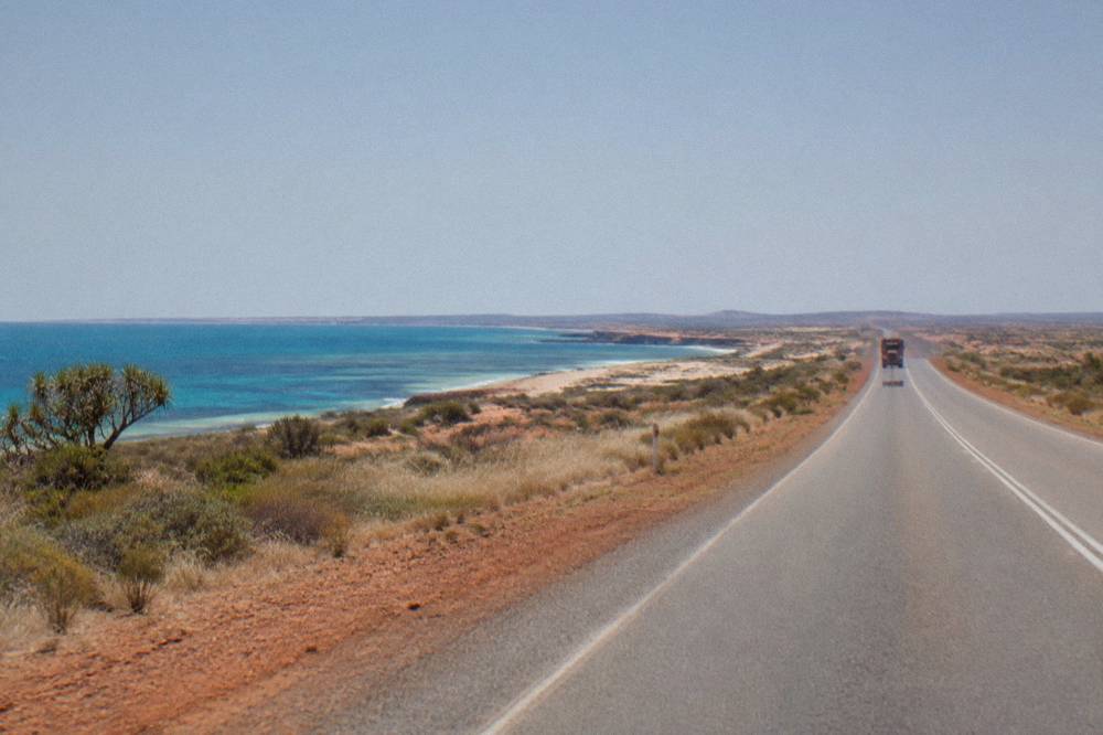 Empty sealed outback highway running north toward Coral Bay under a wide sky
