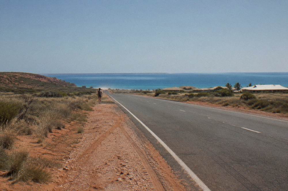 Empty outback road stretching toward the horizon between red dirt and low scrub