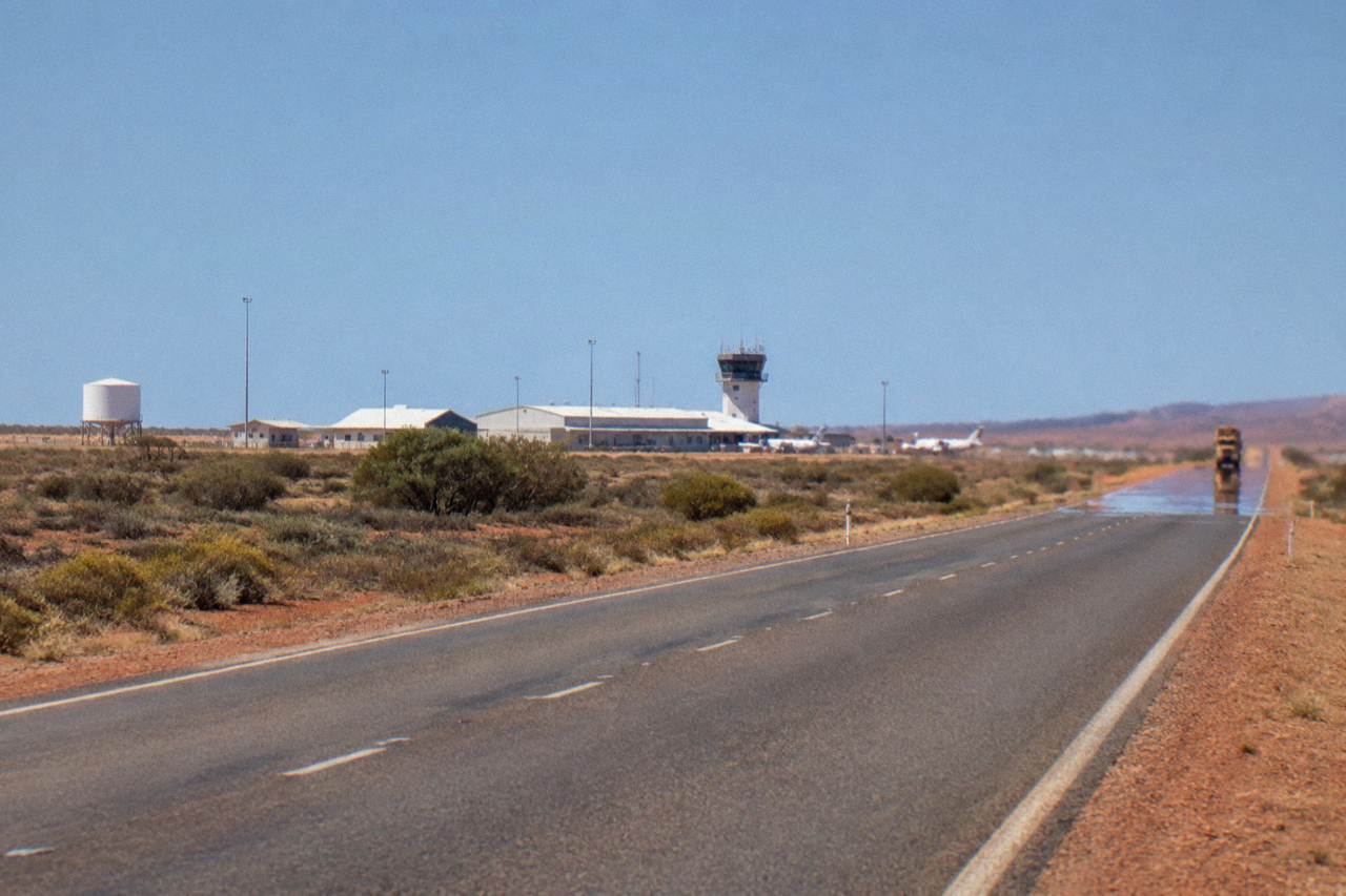 Sealed highway cutting through red desert scrub toward the distant blue water of the Ningaloo coast