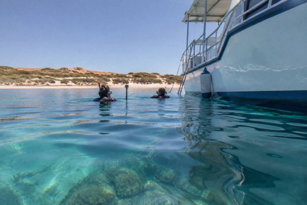 Snorkellers in the water beside a boat over a coral reef lagoon