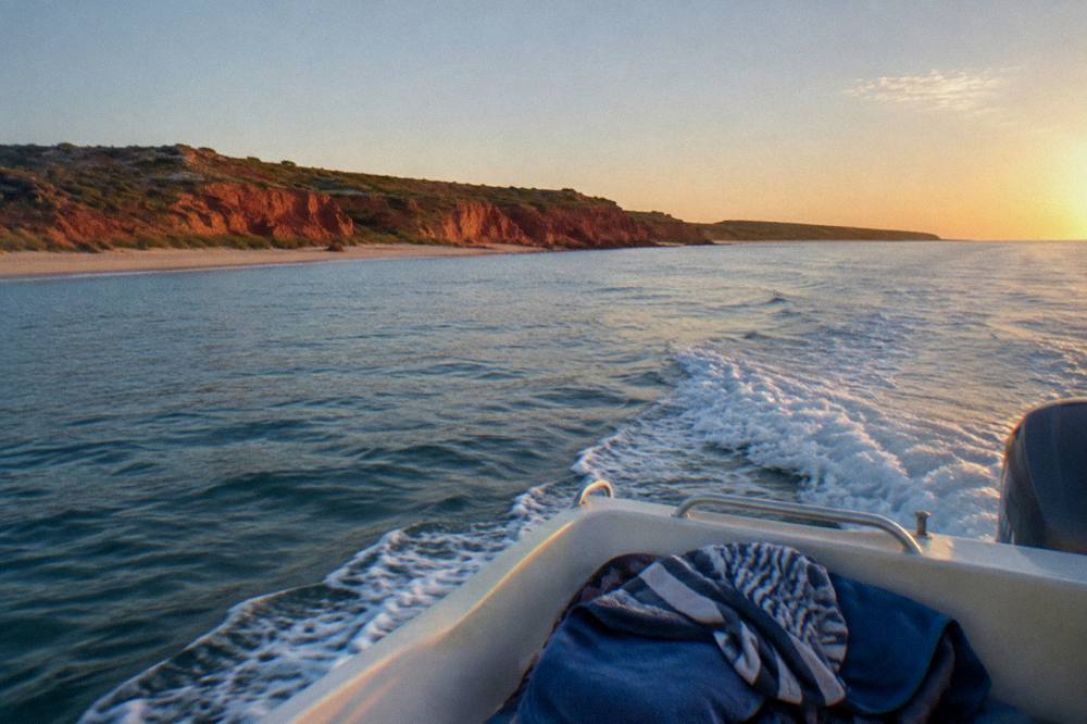 A small charter boat cruising along the Ningaloo coastline in late afternoon light