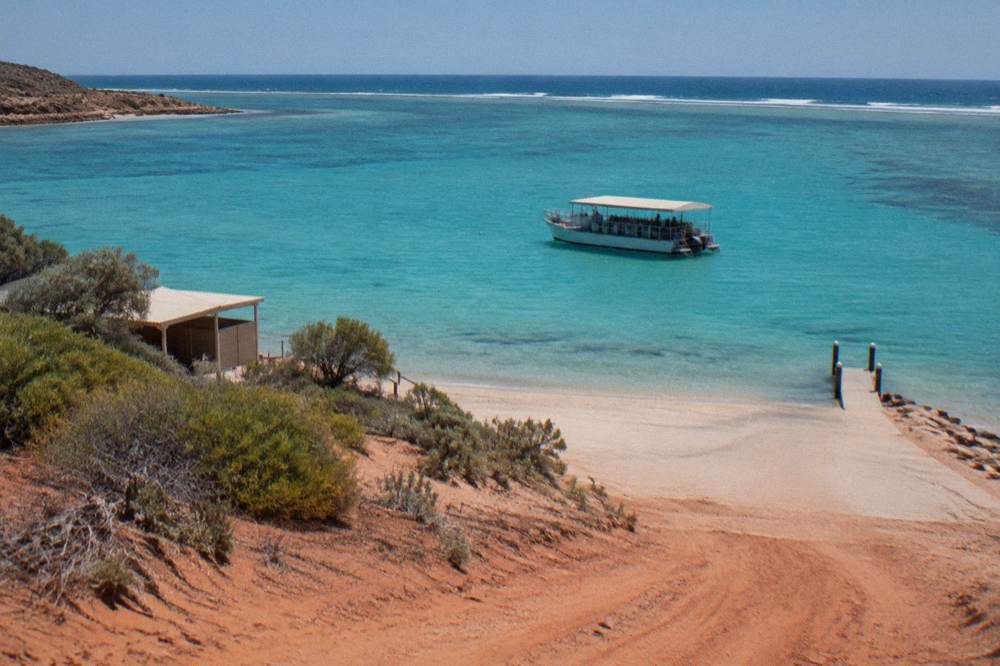 A tour boat anchored over turquoise lagoon water at Ningaloo