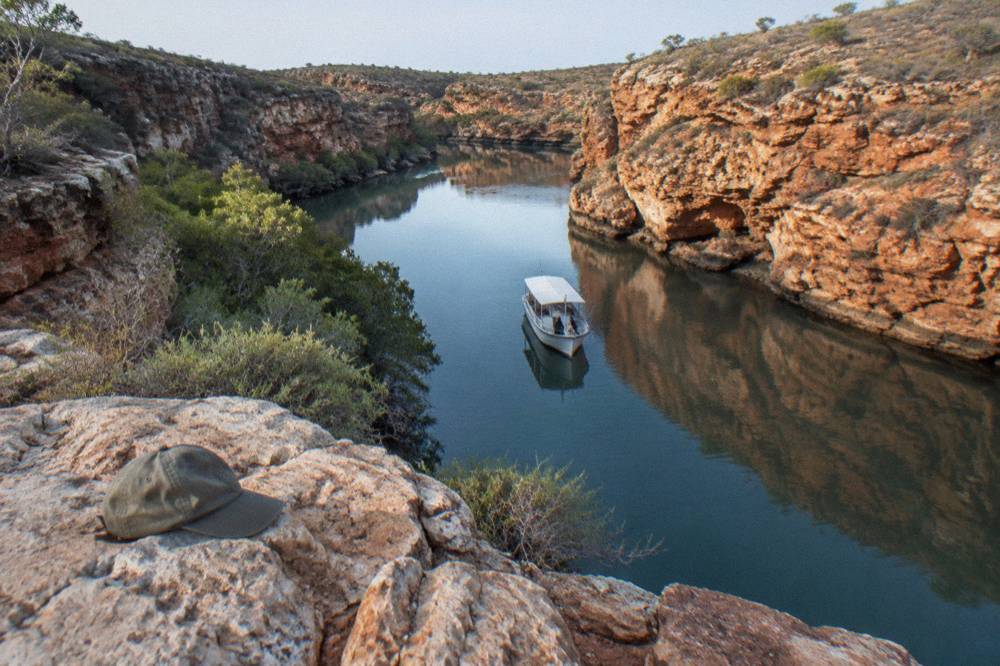A small boat cruising along red limestone cliffs above calm water