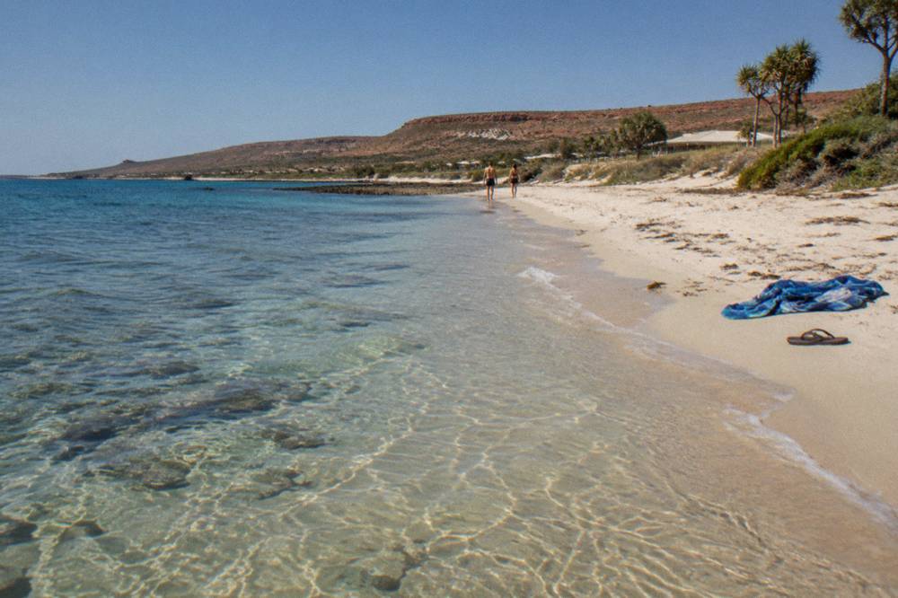 White sand beach meeting clear shallow reef water below low coastal hills