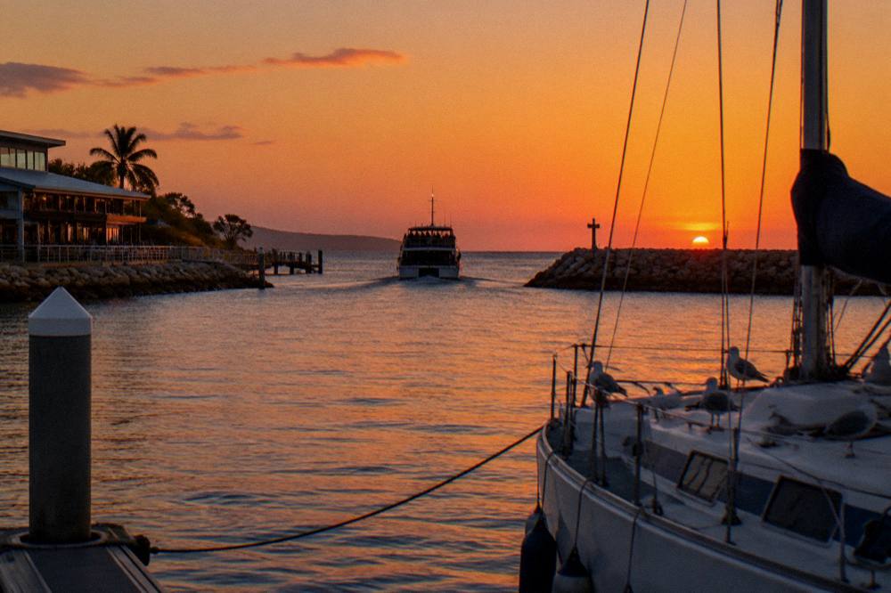 A boat silhouetted against a red sunset over calm sea