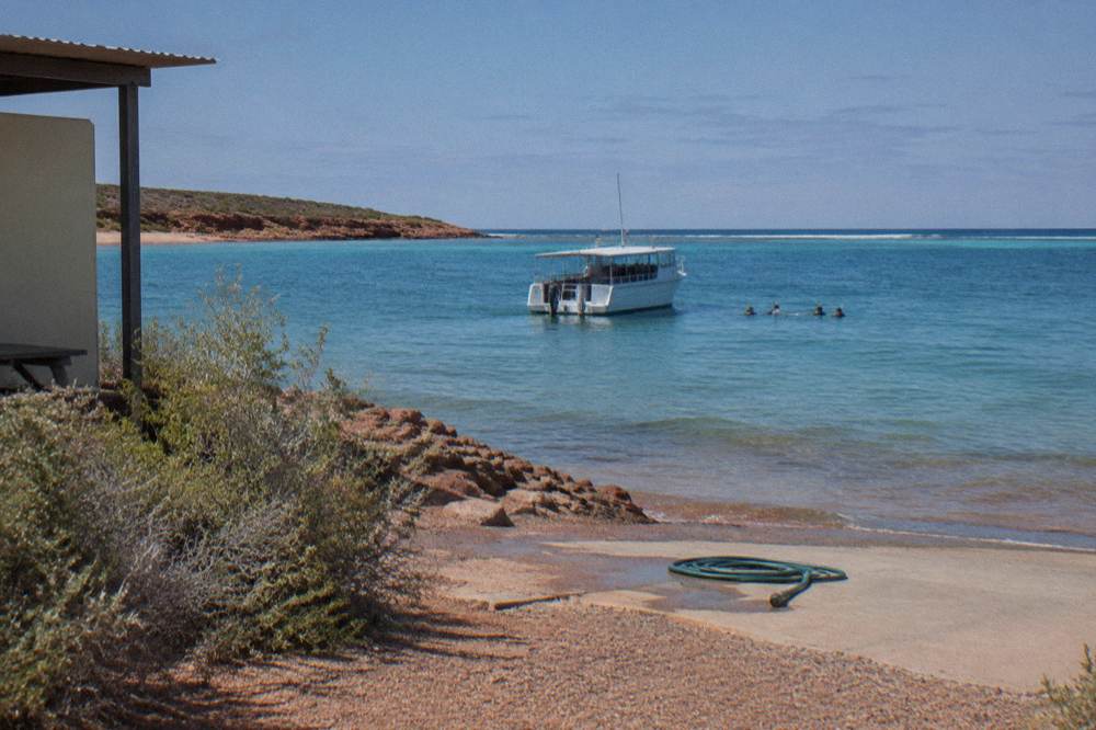 Small boat anchored over shallow reef with snorkellers in the water nearby
