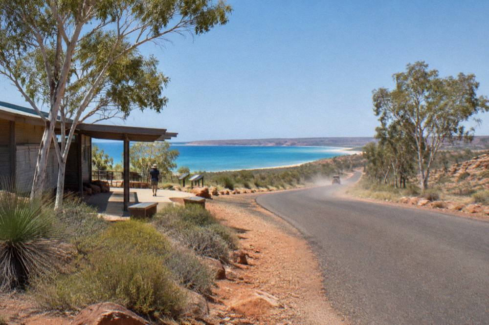 Coastal road through red desert hills toward blue ocean in a national park