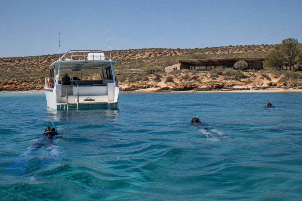 A tour boat anchored in clear blue water while snorkelers wait on the surface at Ningaloo Reef