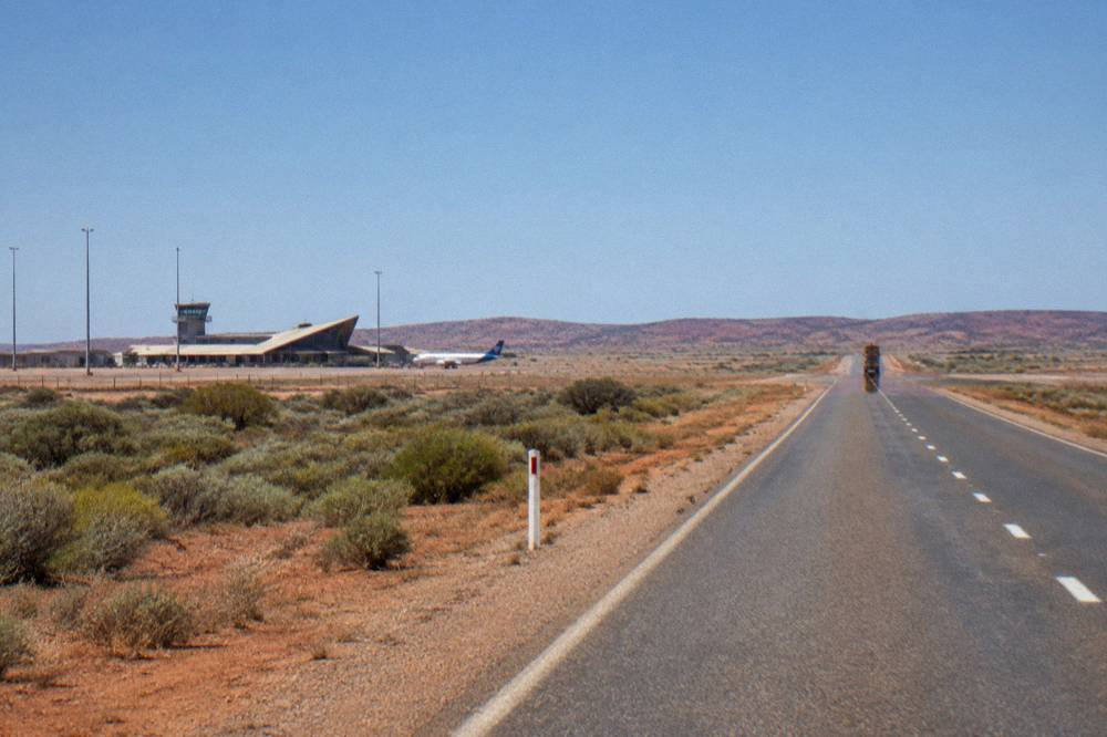 A sealed coastal road running toward low red hills near the North West Cape