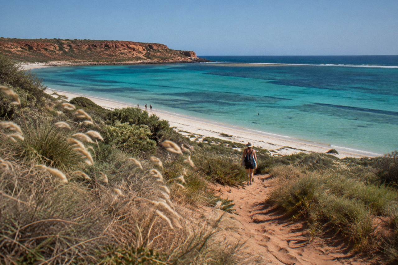 Turquoise lagoon water along a fringing coral reef near a red limestone headland